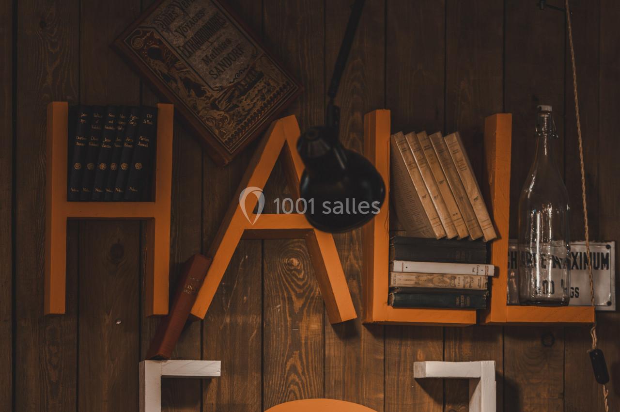 Étagère murale en bois avec des lettres orange formant ’HAL’, décorée de livres, d'une lampe et d'une bouteille en verre.