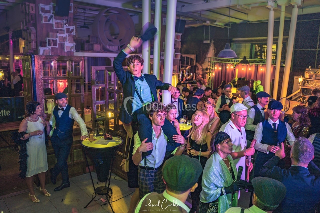 Groupe de personnes en tenue rétro dans une ambiance festive, avec un homme porté sur les épaules au centre.