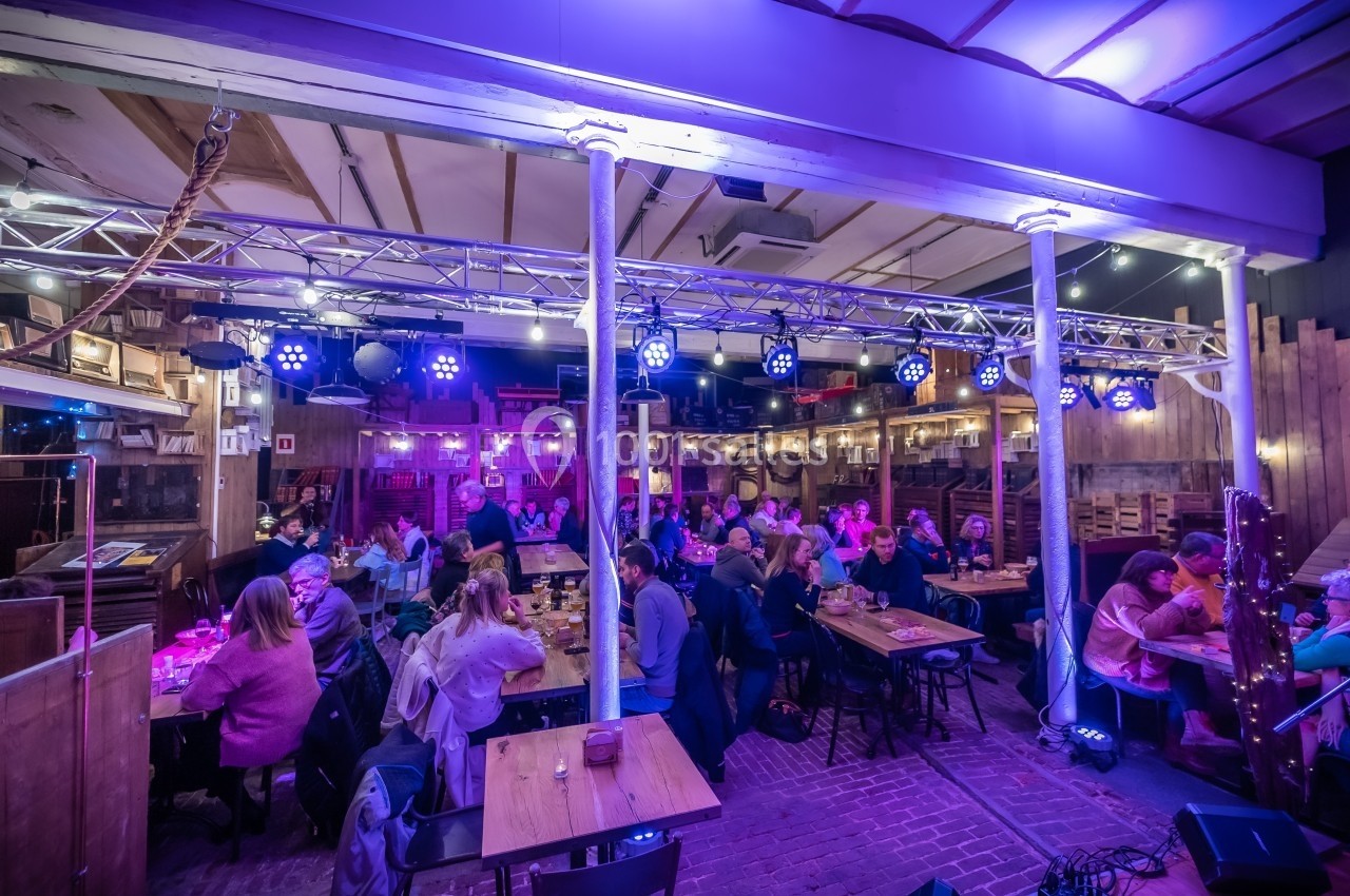 Salle de restaurant animée avec des convives attablés sous un éclairage violet et une structure lumineuse suspendue.