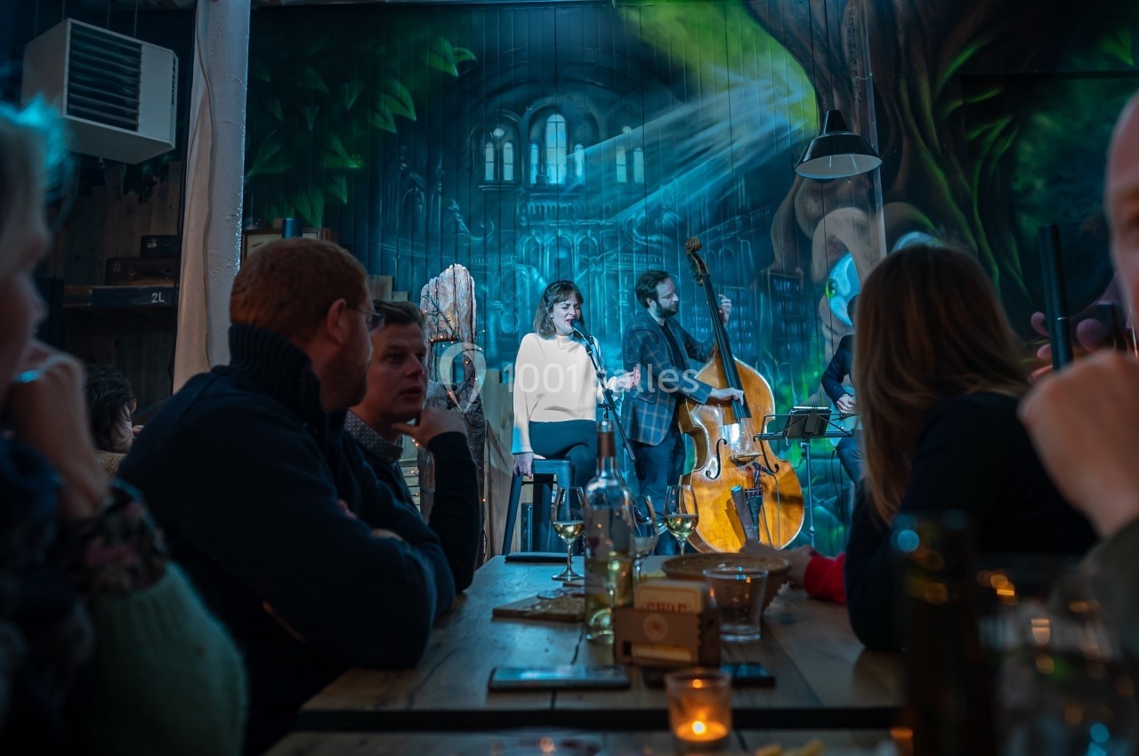 Un groupe joue de la musique live dans un café, avec une chanteuse et un contrebassiste sur une scène éclairée.