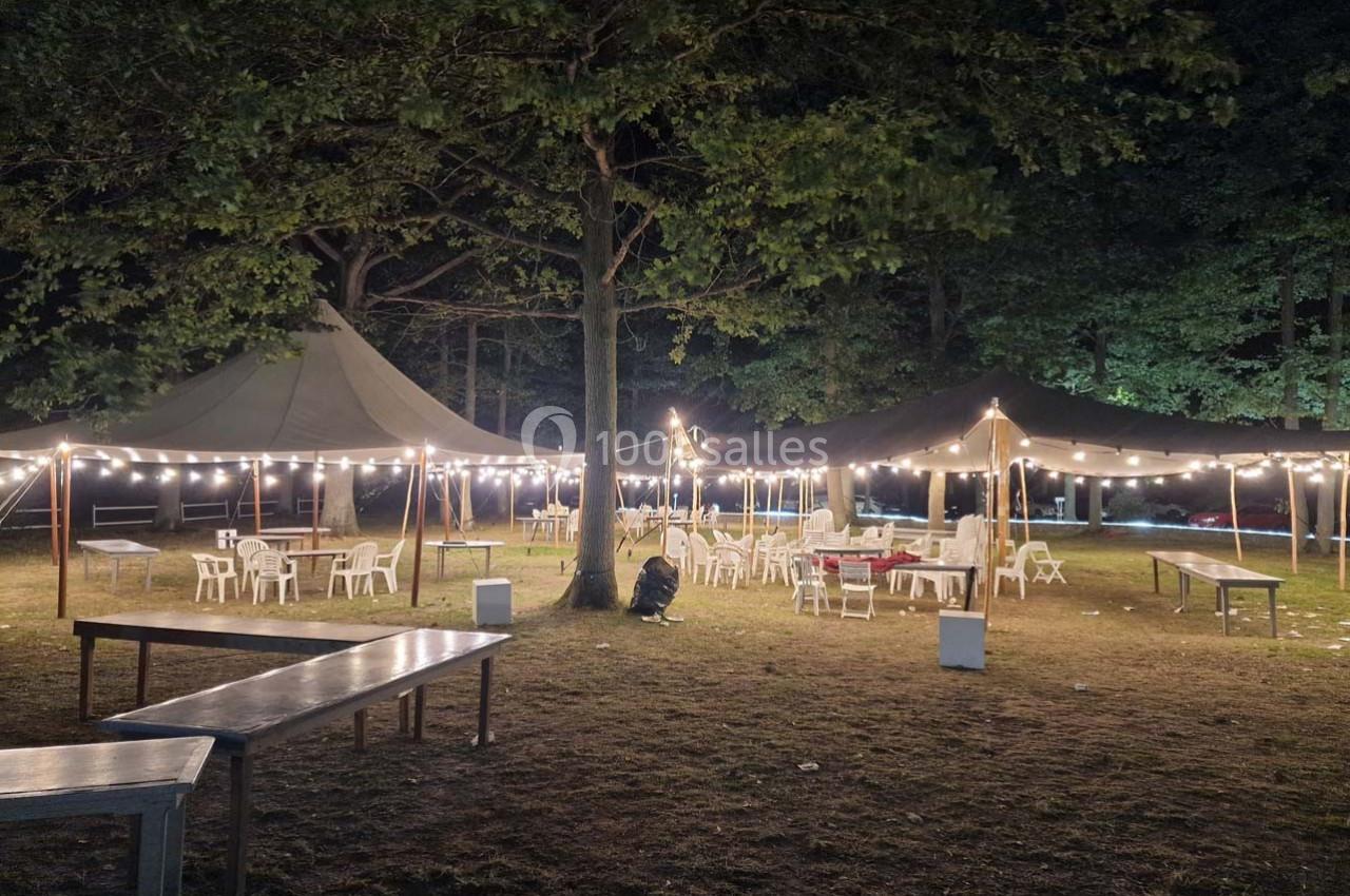 Tentes éclairées par des guirlandes lumineuses dans un espace extérieur avec des tables et des chaises disposées sur l'herbe.