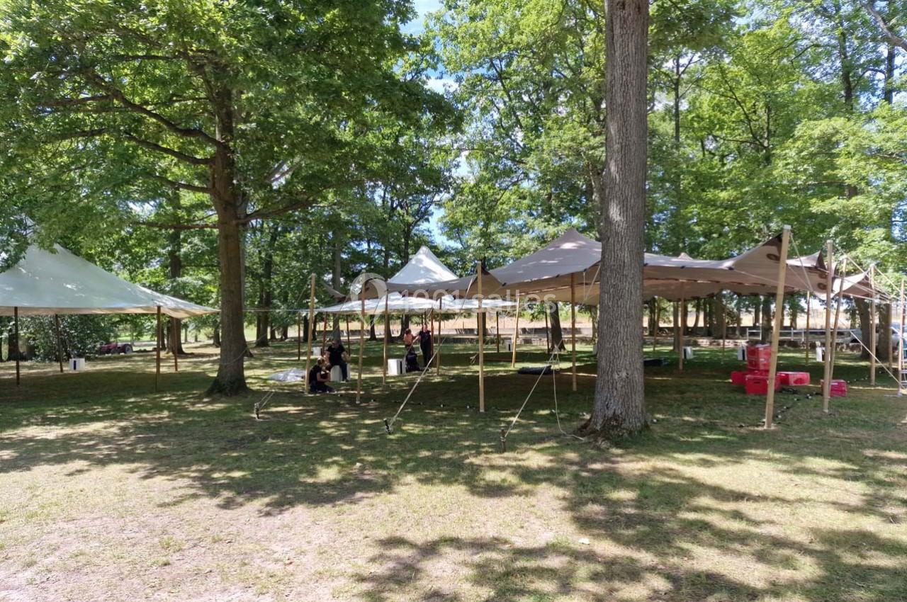Tentes installées dans une clairière ombragée avec quelques personnes assises sous l'une d'elles.
