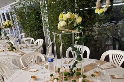 Deux tables rondes décorées pour un événement, avec nappes blanches, fleurs, verres et serviettes pliées.