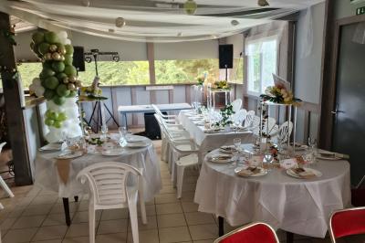 Deux tables rondes décorées pour un événement, avec nappes blanches, fleurs, verres et serviettes pliées.