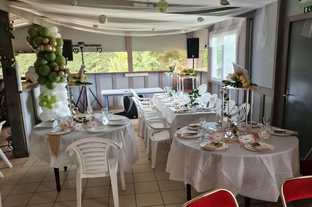Salle décorée pour un événement avec tables rondes dressées, chaises blanches, ballons et compositions florales.