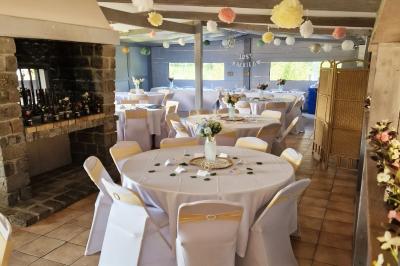 Deux tables rondes décorées pour un événement, avec nappes blanches, fleurs, verres et serviettes pliées.