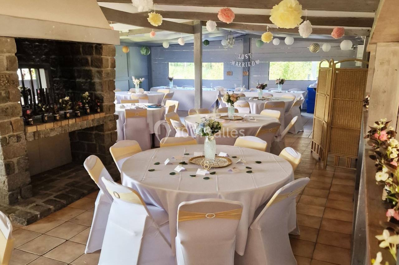 Salle décorée pour une réception avec tables rondes dressées, chaises blanches et ornements suspendus.