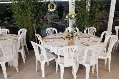 Deux tables rondes décorées pour un événement, avec nappes blanches, fleurs, verres et serviettes pliées.