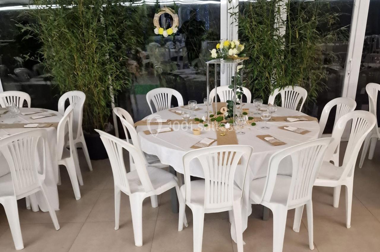 Table ronde décorée pour un événement, entourée de chaises blanches, avec centre de table floral et bambous en arrière-plan.