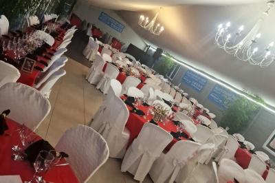 Deux tables rondes décorées pour un événement, avec nappes blanches, fleurs, verres et serviettes pliées.