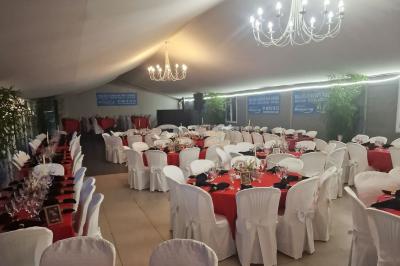 Deux tables rondes décorées pour un événement, avec nappes blanches, fleurs, verres et serviettes pliées.