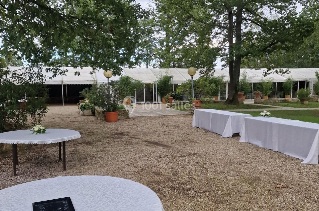 Espace extérieur avec tables dressées, allée gravillonnée, tentes blanches et végétation environnante.