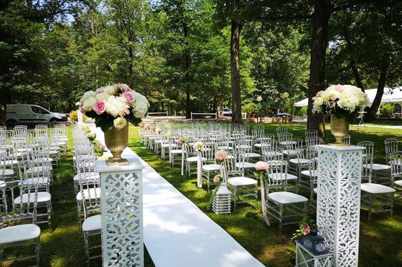 Allée centrale décorée de fleurs, entourée de chaises transparentes, dans un jardin pour une cérémonie en plein air.