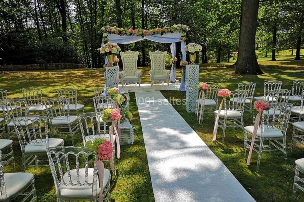 Allée centrale bordée de chaises décorées de fleurs menant à une arche ornée pour une cérémonie en plein air.