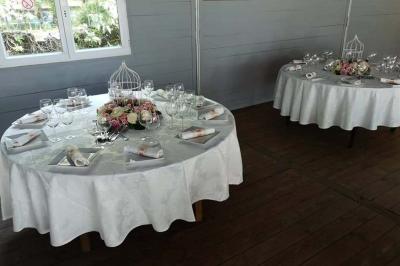 Deux tables rondes décorées pour un événement, avec nappes blanches, fleurs, verres et serviettes pliées.