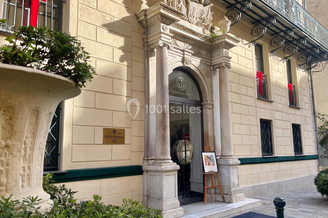 Façade d'un bâtiment élégant avec une entrée ornée de colonnes, des décorations et des plantes environnantes.