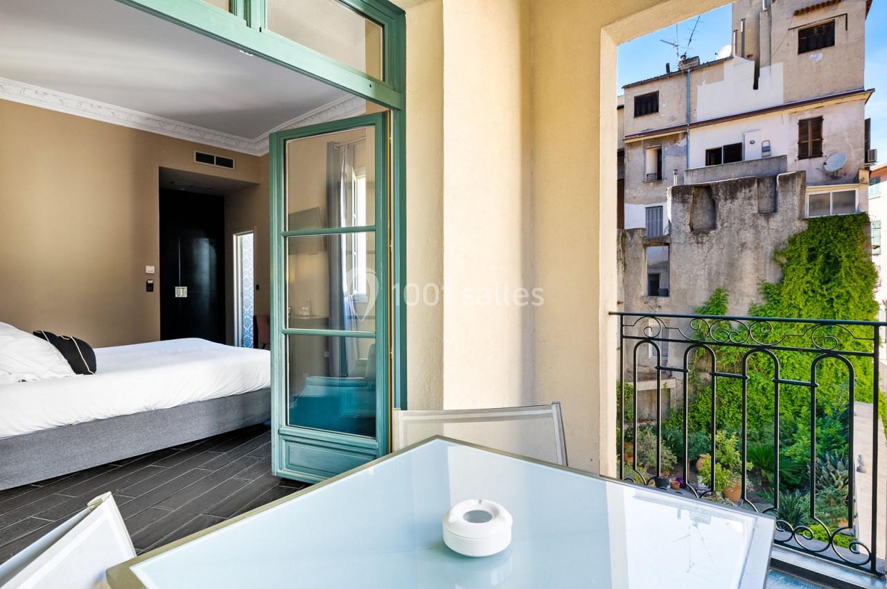 Vue d'une chambre d'hôtel avec lit, balcon aménagé et vue sur des bâtiments et un jardin urbain.
