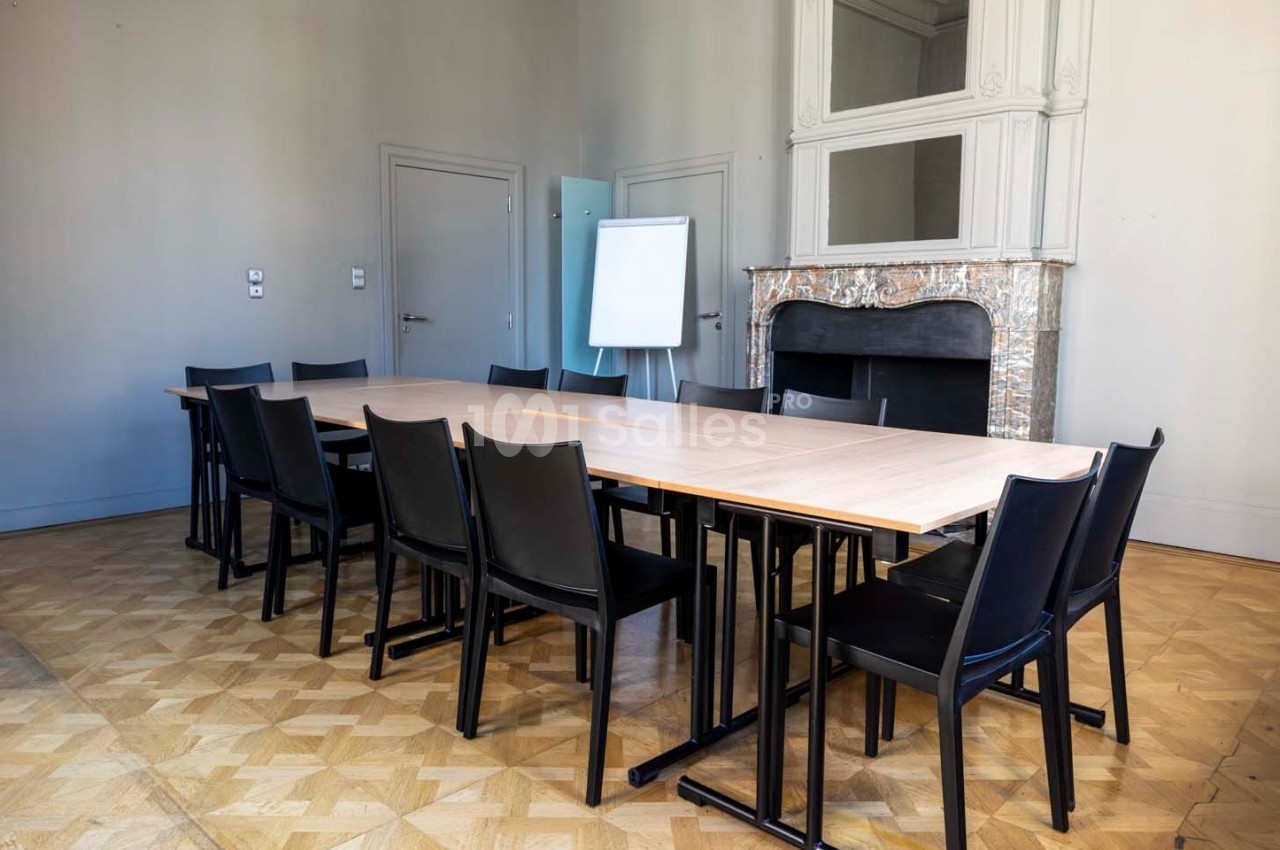 Salle de réunion avec une grande table en bois, des chaises noires, un tableau blanc et une cheminée décorative.