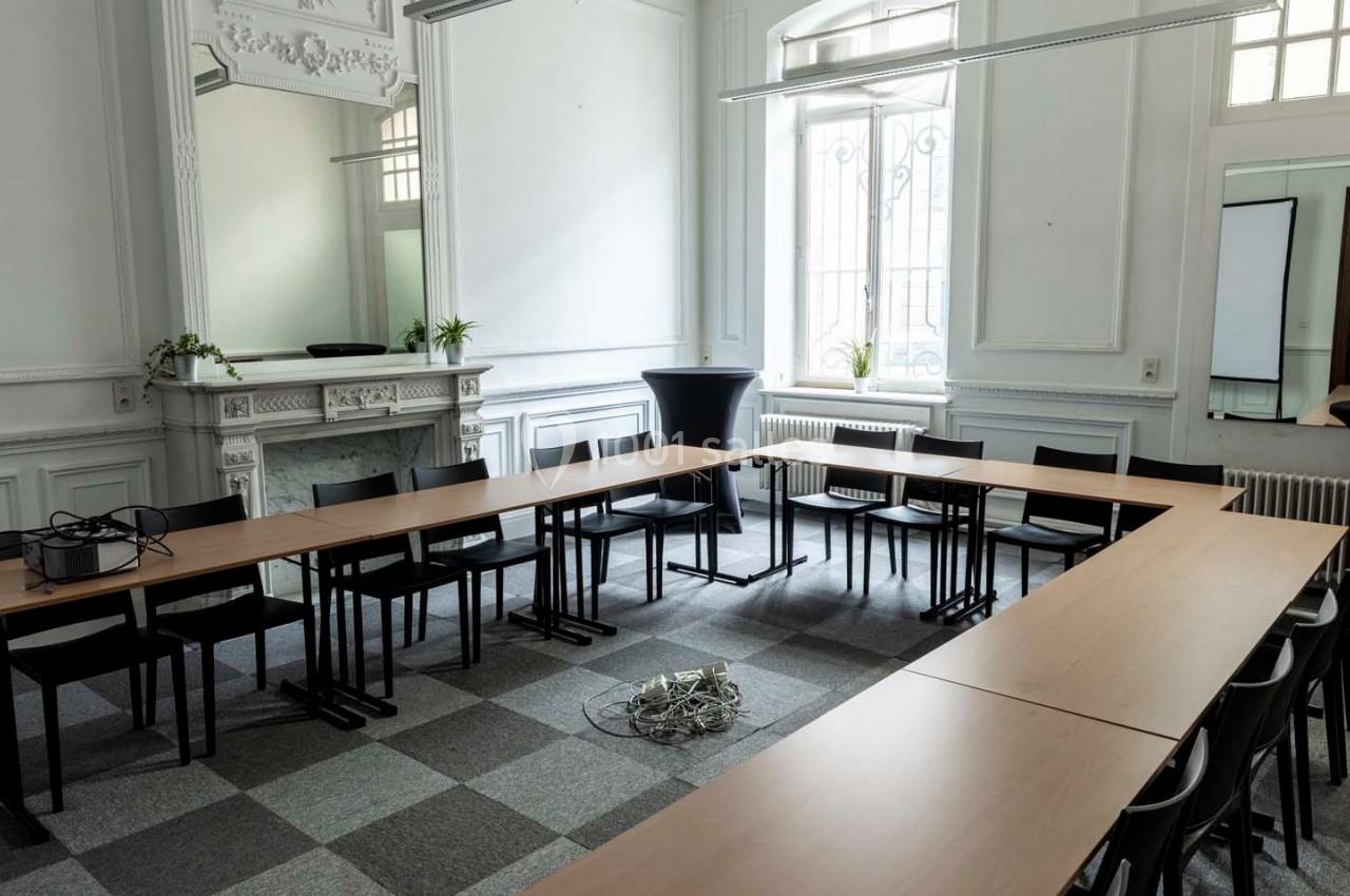 Salle de réunion lumineuse avec des tables disposées en U, des chaises noires et un amas de câbles au sol.
