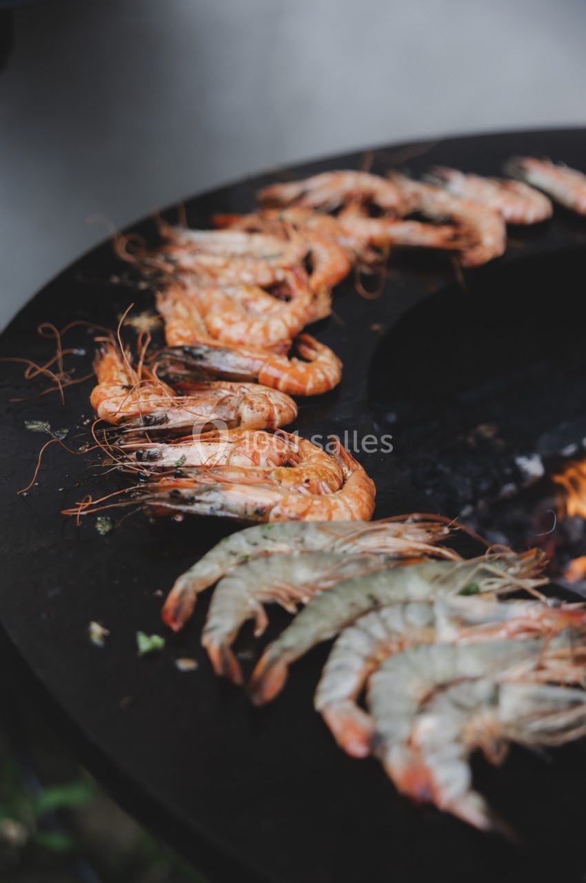 Crevettes crues et grillées disposées sur une plaque de cuisson ronde au-dessus d'un feu.