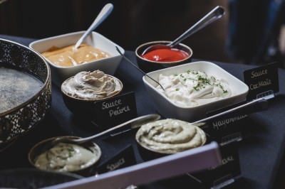 Assortiment de sauces variées dans des bols avec étiquettes, disposées sur une table sombre.