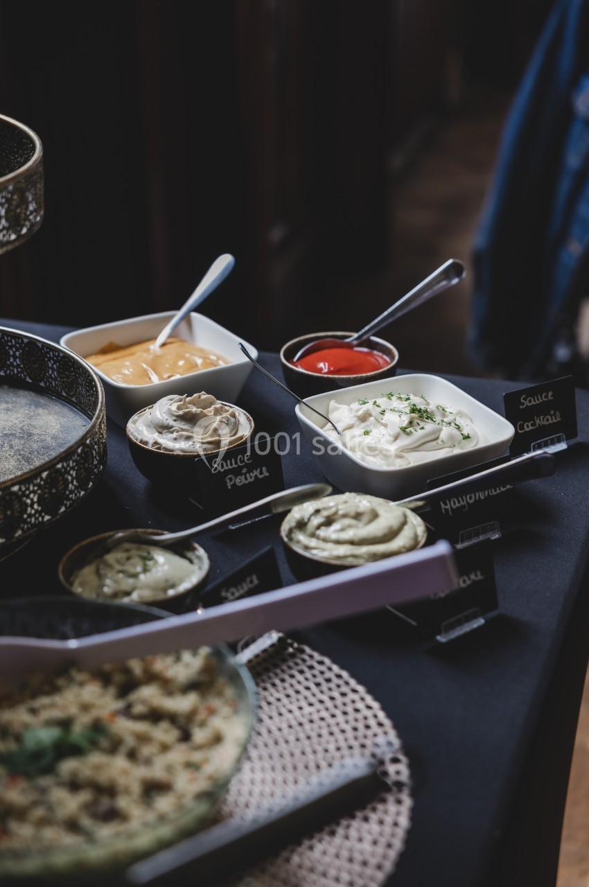 Assortiment de sauces variées dans des bols avec étiquettes, disposées sur une table sombre.