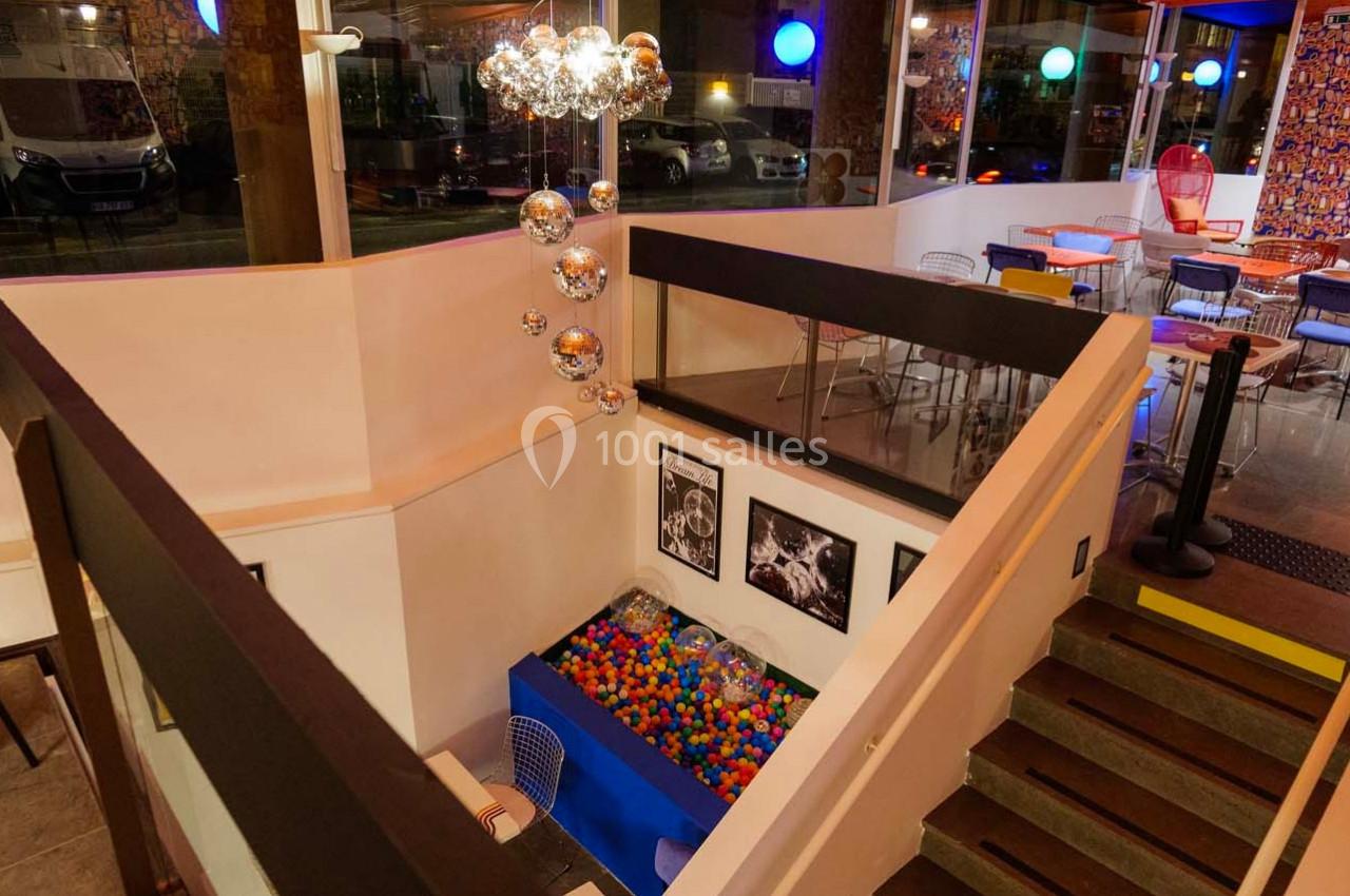 Intérieur d'un espace moderne avec une piscine à balles colorées, des tables et des chaises dans un décor lumineux.