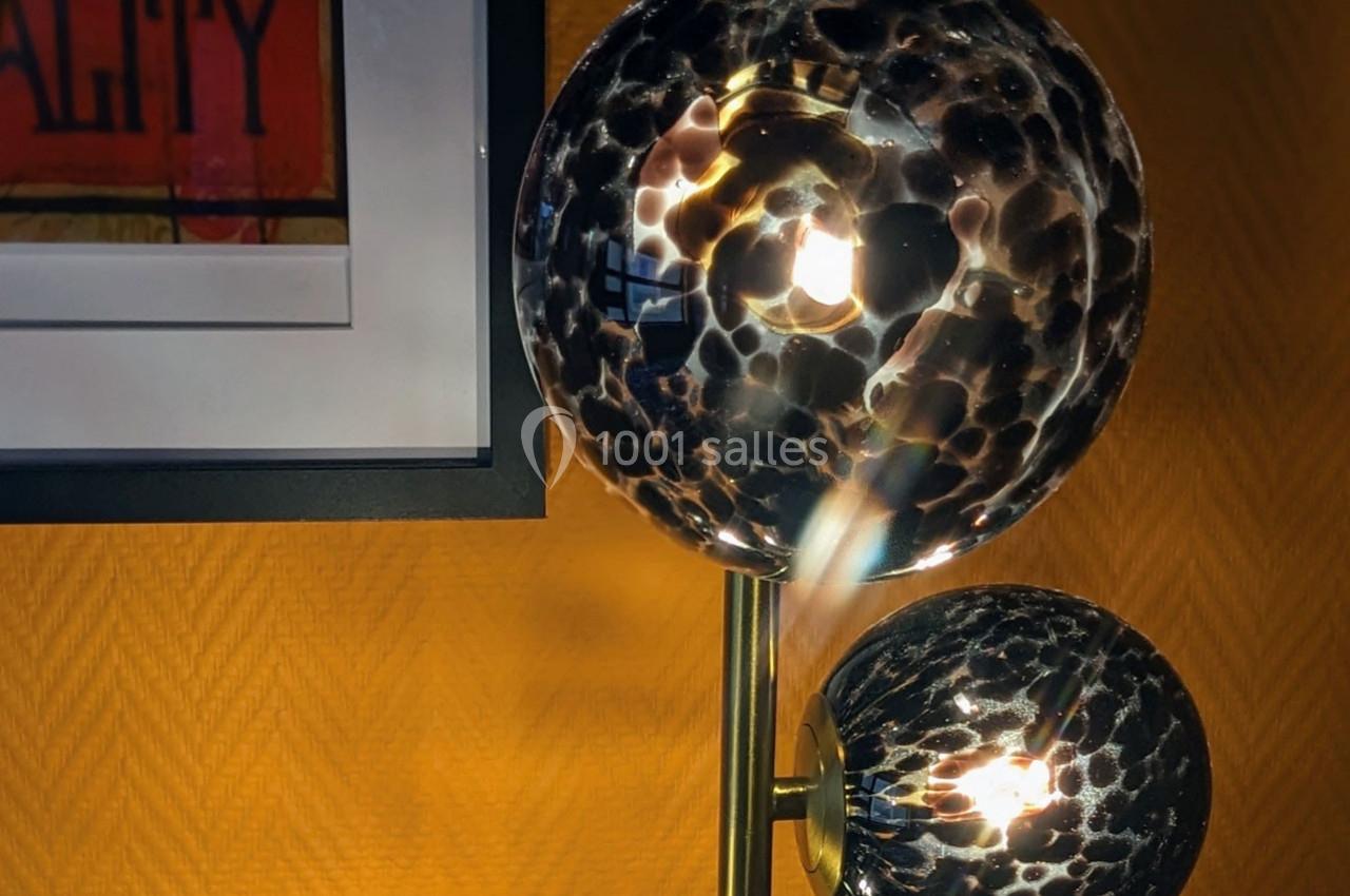 Lampe à globes en verre texturé noir et doré, allumée, devant un mur jaune avec un cadre accroché.