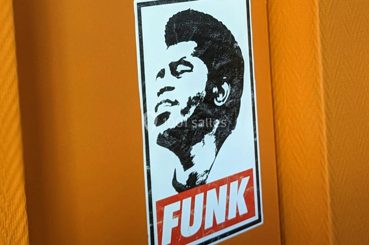 Autocollant en noir et blanc d'un visage stylisé avec le mot ’FUNK’ en rouge sur un mur orange.