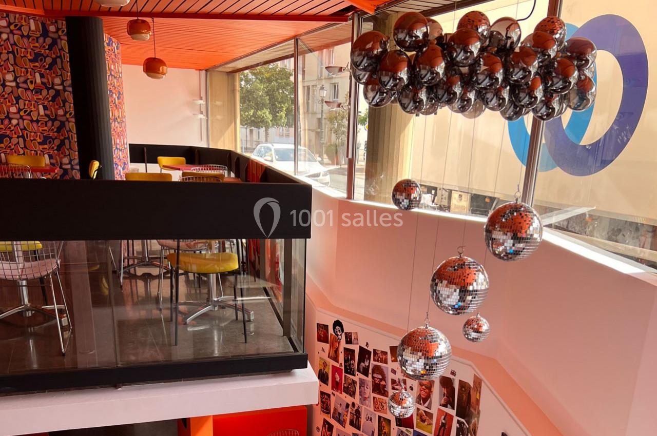 Intérieur coloré d'un café moderne avec mezzanine, décorations murales vives et lustre en boules miroir.