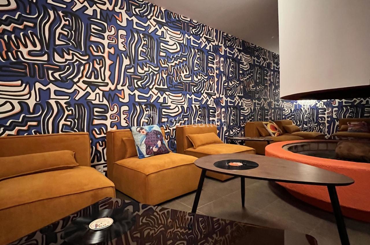 Salon moderne avec fauteuils jaunes, table basse noire et murs décorés de motifs abstraits bleus et blancs.