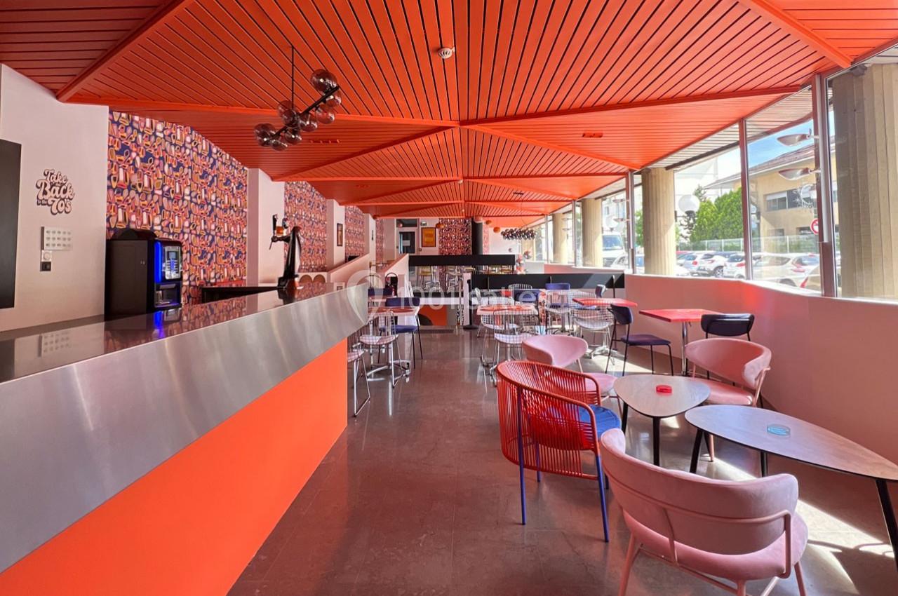 Salle lumineuse avec comptoir orange, tables et chaises modernes, murs décorés de motifs colorés.