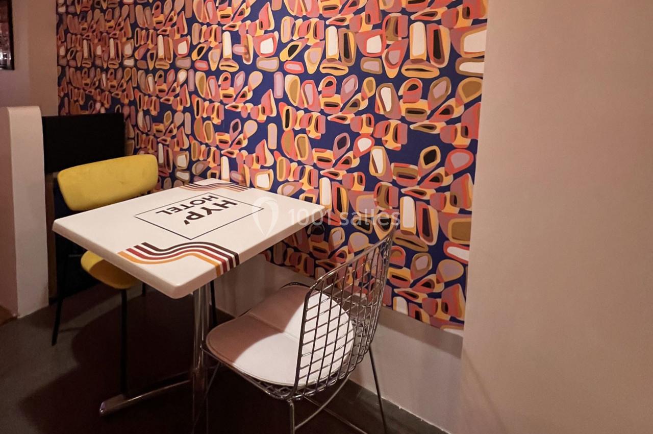 Table et deux chaises dans un coin de pièce, avec un mur décoré d’un papier peint coloré à motifs géométriques.