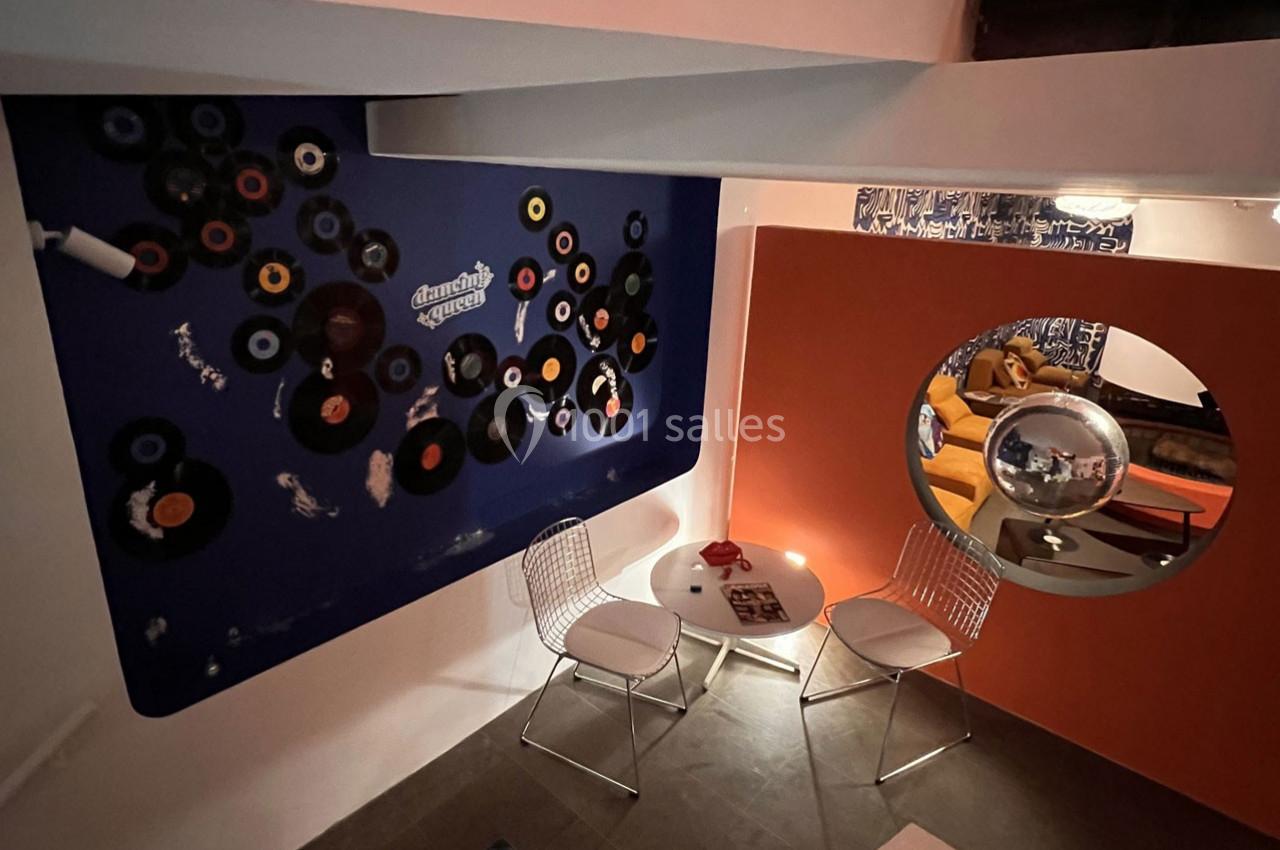 Mur décoré de vinyles, petite table ronde avec deux chaises, ambiance rétro dans un espace intérieur coloré.