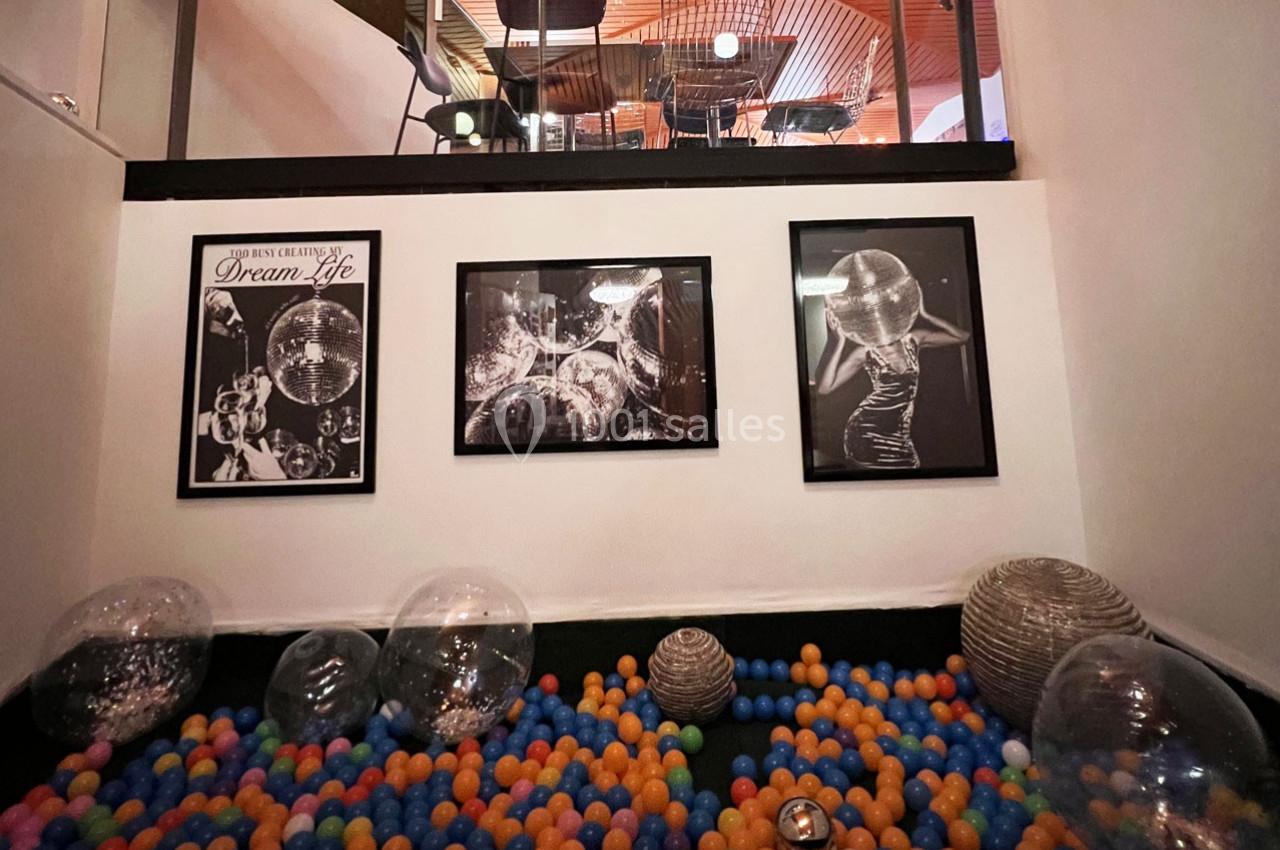 Piscine à balles colorées avec des ballons transparents, décorée de photos en noir et blanc sur un mur blanc.