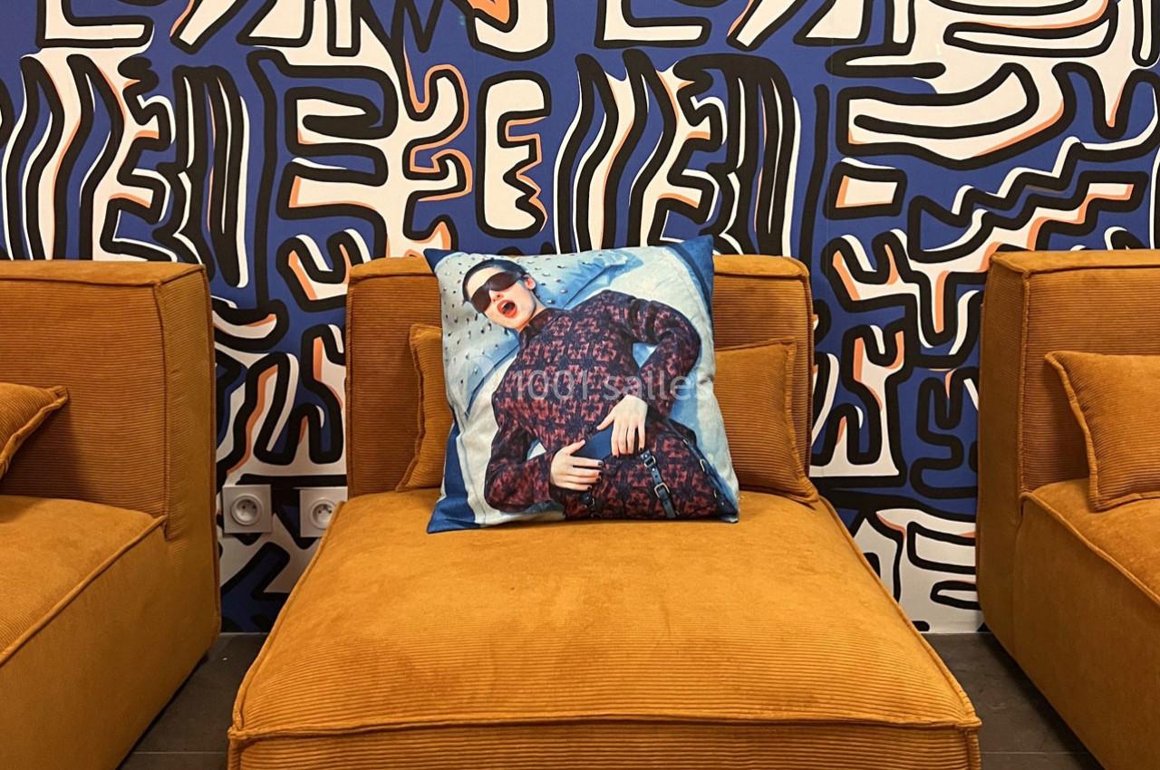 Fauteuil en velours orange avec un coussin décoratif imprimé, devant un mur à motifs abstraits bleu et noir.