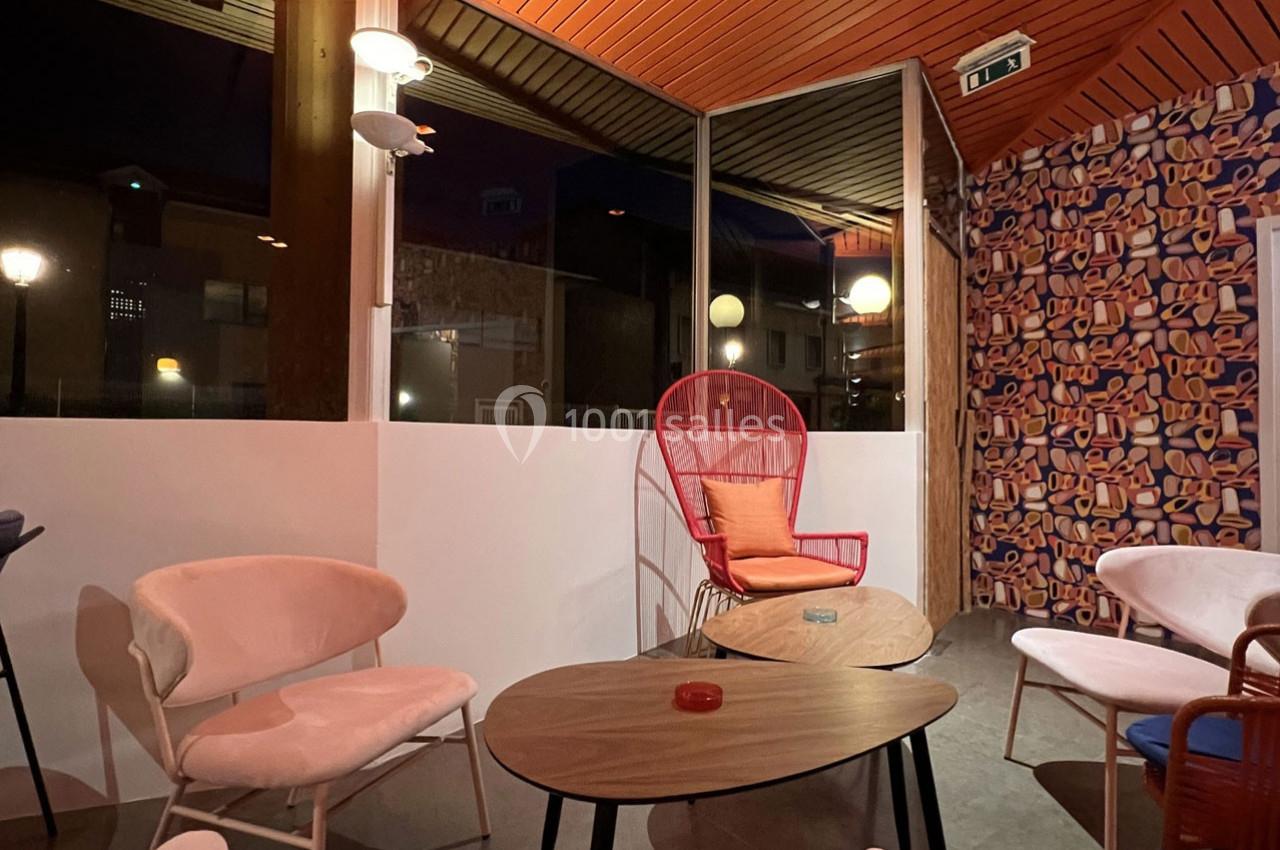 Espace intérieur avec des fauteuils colorés, des tables basses en bois et une décoration murale vive, éclairé en soirée.