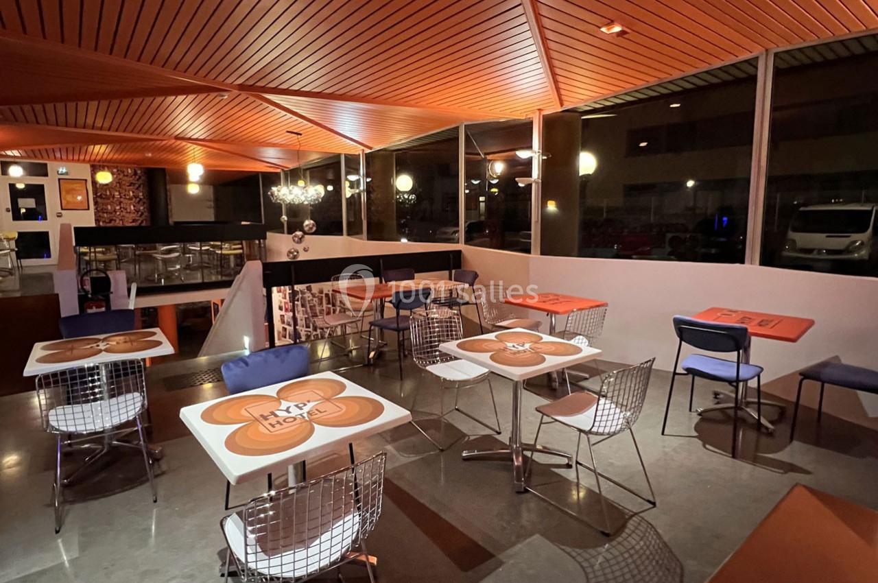 Salle de restaurant moderne avec tables décorées, chaises en métal et éclairage chaleureux en soirée.
