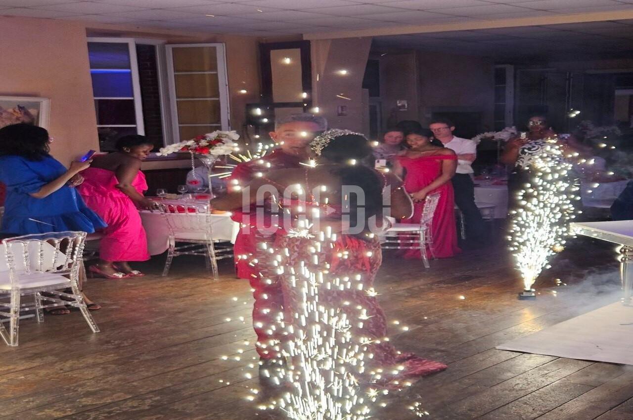 Des invités en tenue de soirée dansent au milieu de jets d'étincelles dans une salle décorée pour un événement.