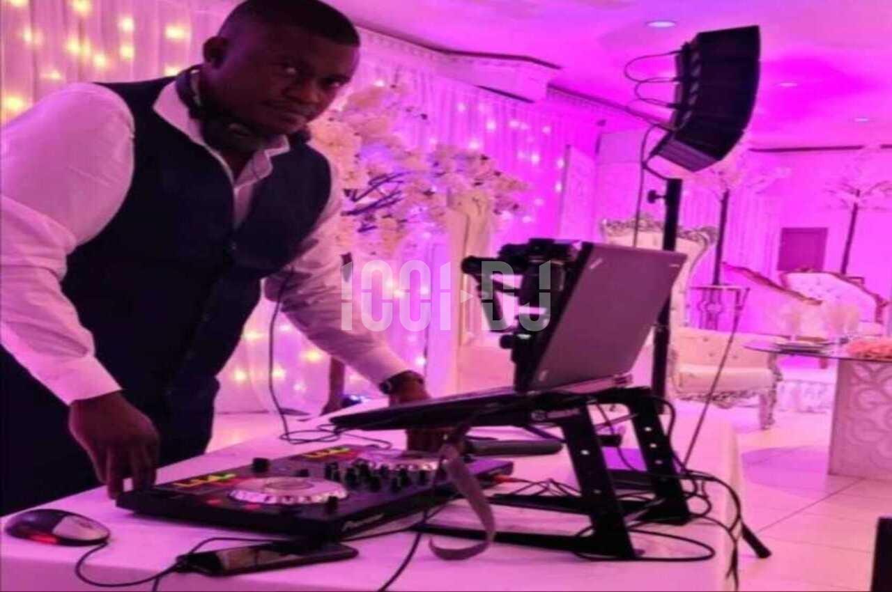 Un DJ en costume utilise une table de mixage et un ordinateur dans une salle décorée avec des lumières roses.
