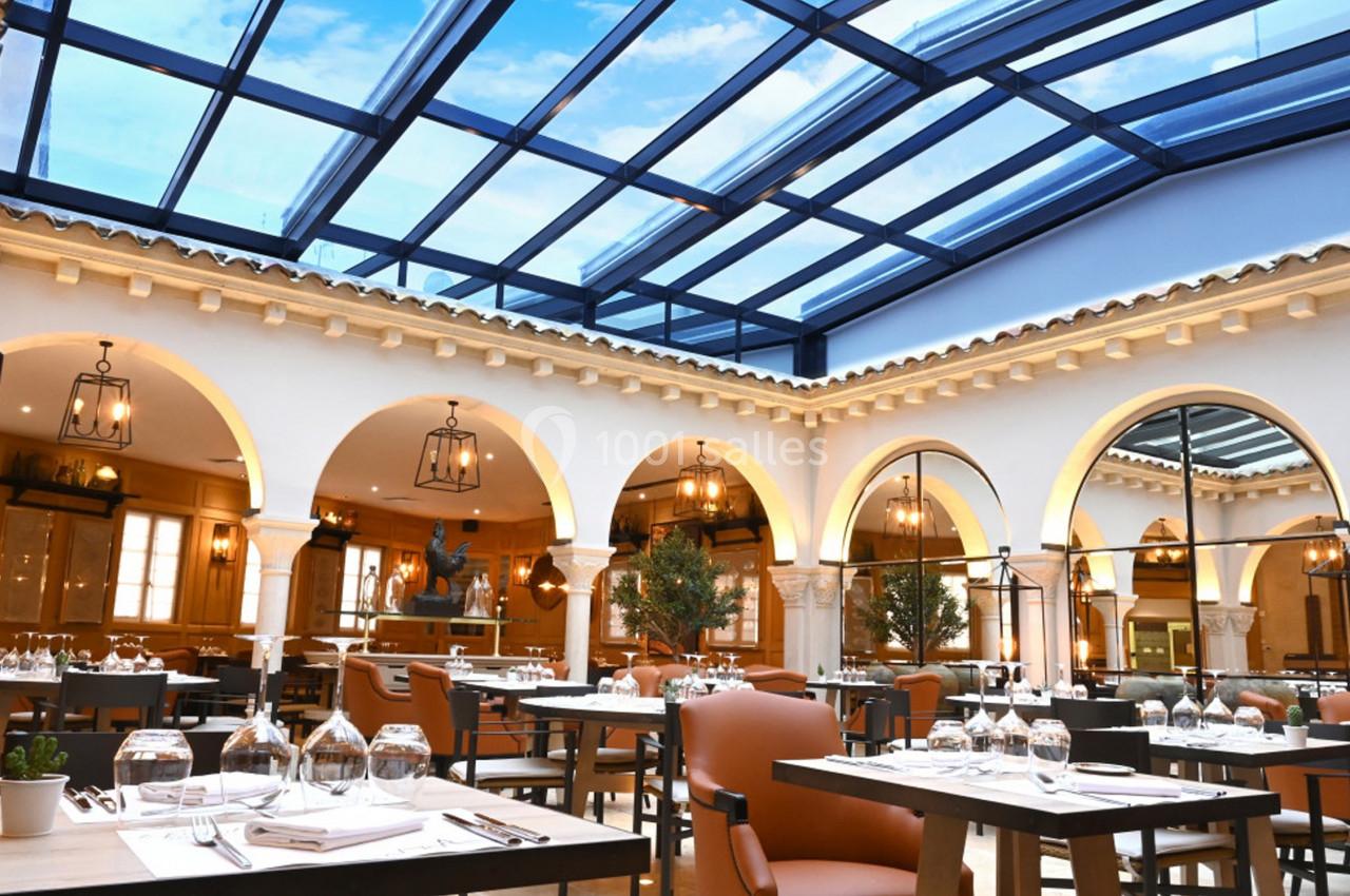 Salle de restaurant lumineuse avec verrière, tables dressées et arches décoratives dans un style méditerranéen.