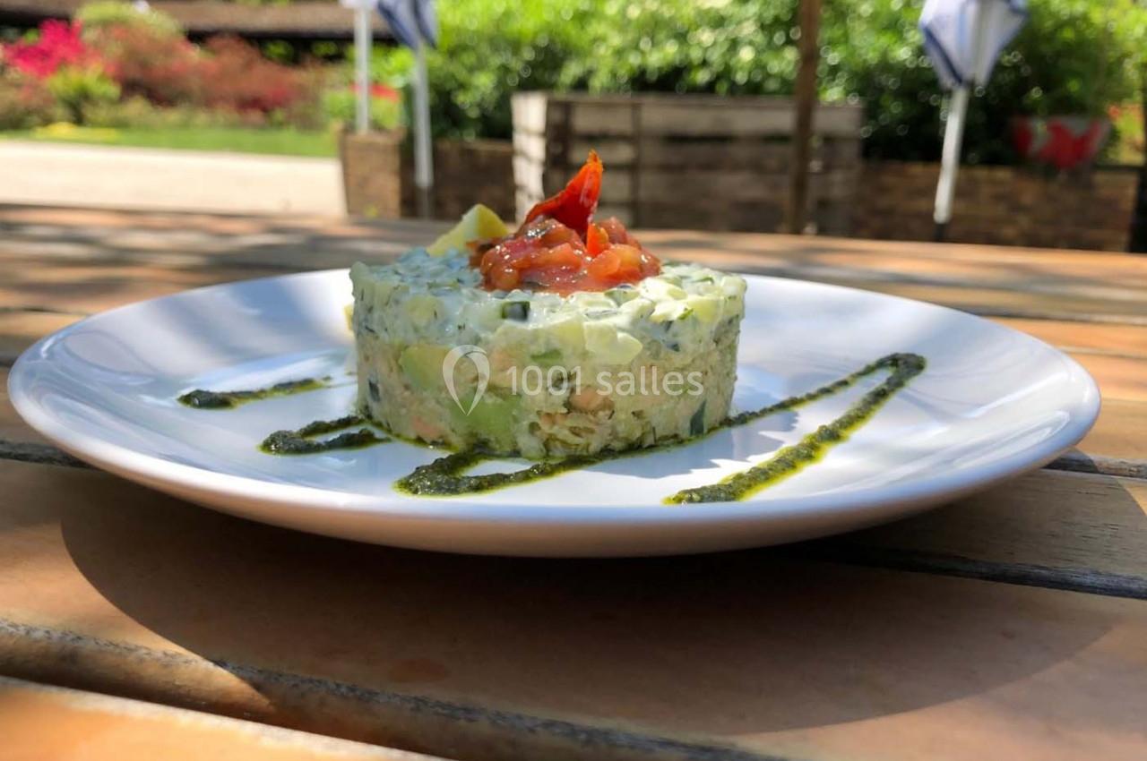 Tartare de légumes frais avec une garniture de tomates, présenté sur une assiette blanche en extérieur.