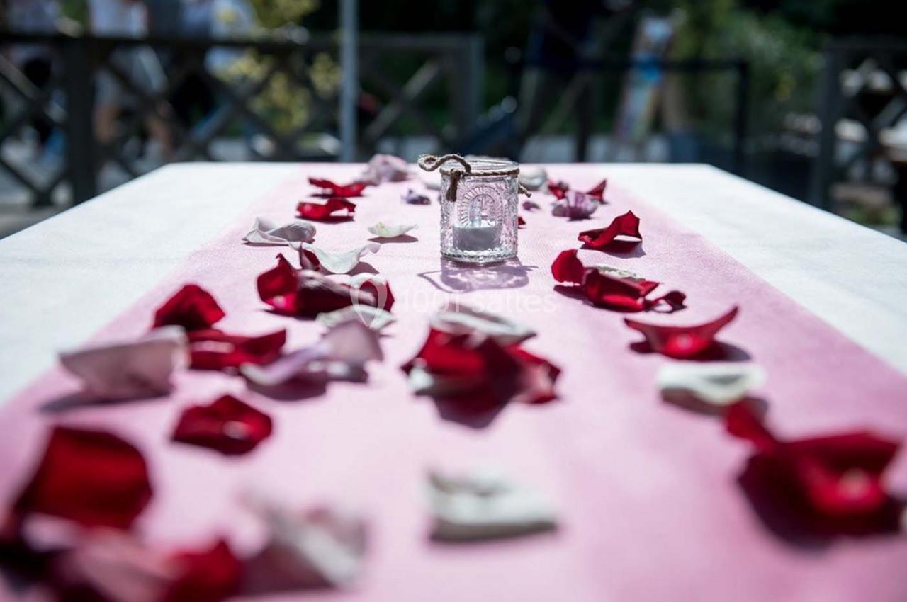 Pétales rouges et blancs dispersés sur une nappe rose avec un photophore en verre au centre.