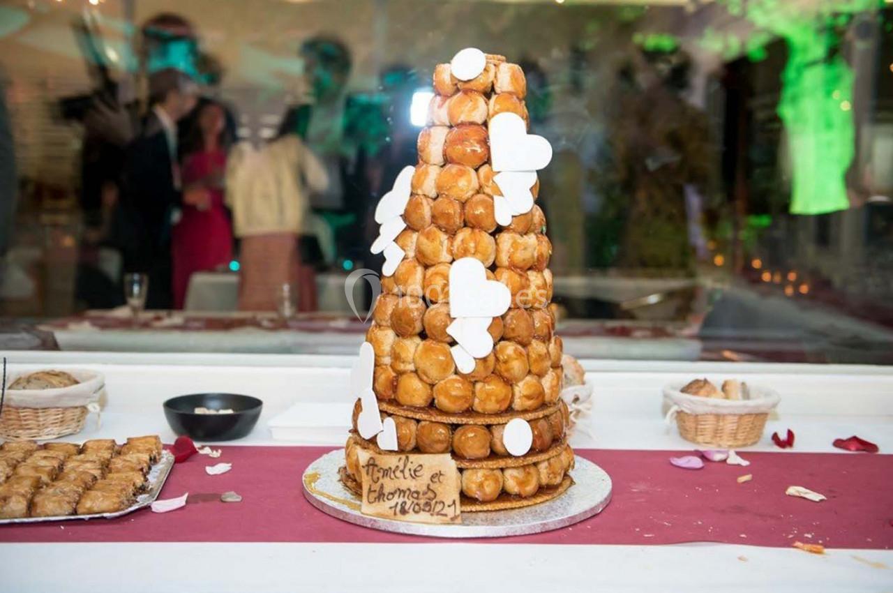 Pièce montée en choux décorée de cœurs blancs, posée sur une table avec nappes rouges et desserts autour.