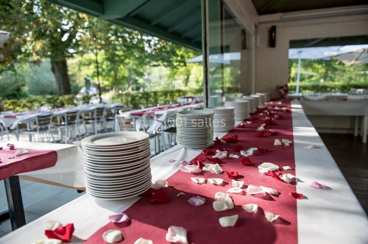 Pile d'assiettes sur une table décorée de pétales de rose, dans une salle lumineuse avec vue sur un jardin.