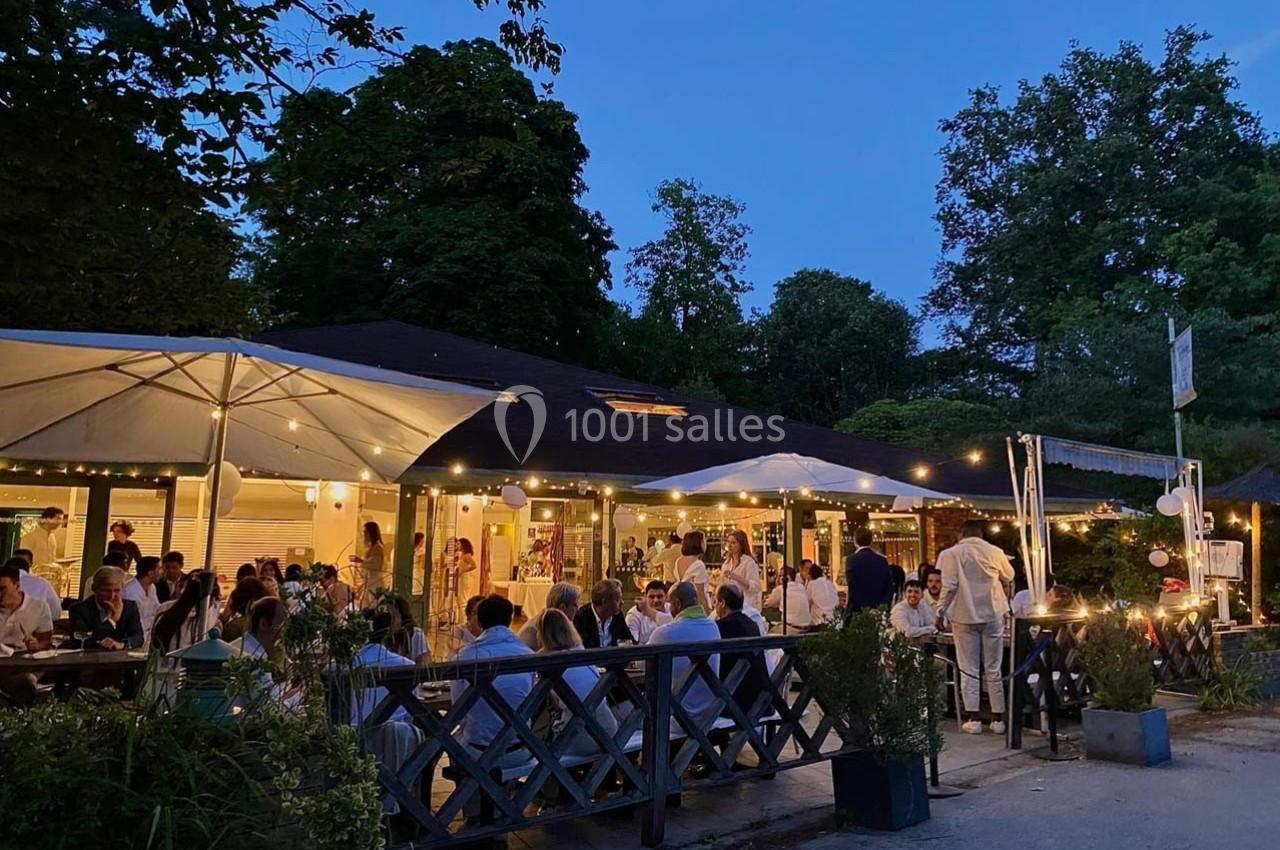 Terrasse d'un restaurant éclairée en soirée, avec des convives attablés sous des parasols et des guirlandes lumineuses.