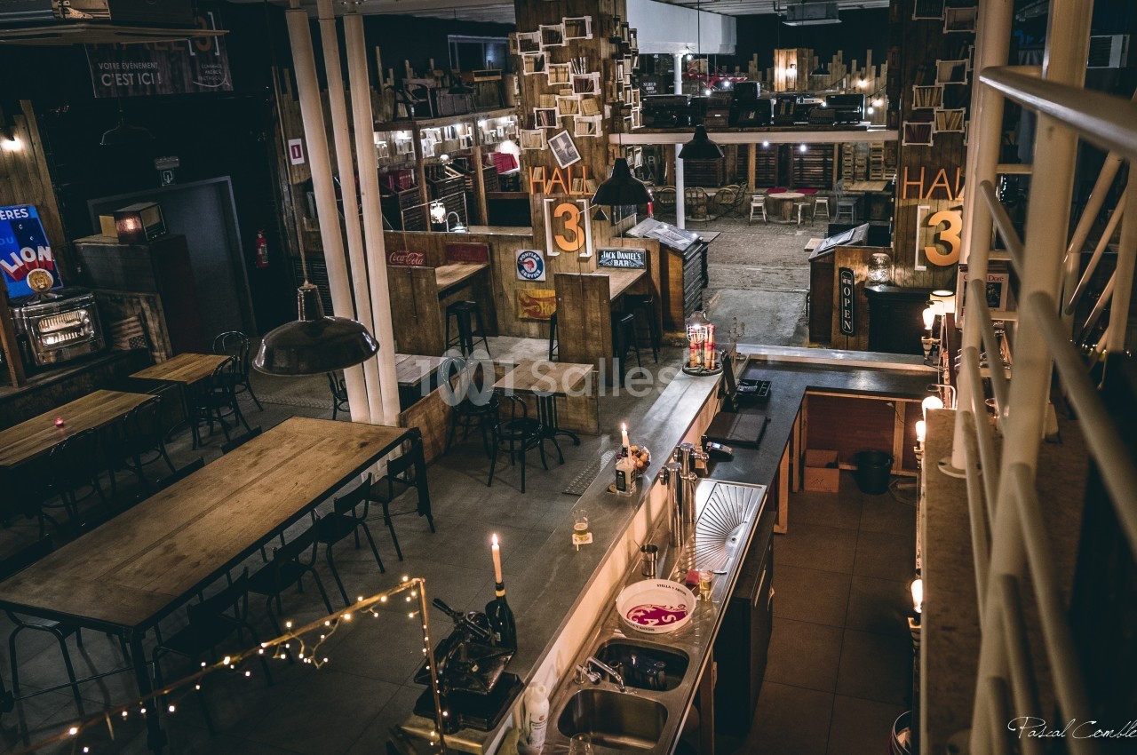 Vue d'un espace intérieur industriel avec des tables en bois, un bar et une ambiance chaleureuse et tamisée.