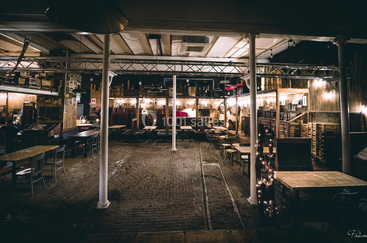 Salle intérieure d'un café ou restaurant avec tables, chaises et éclairage tamisé, ambiance chaleureuse et rustique.