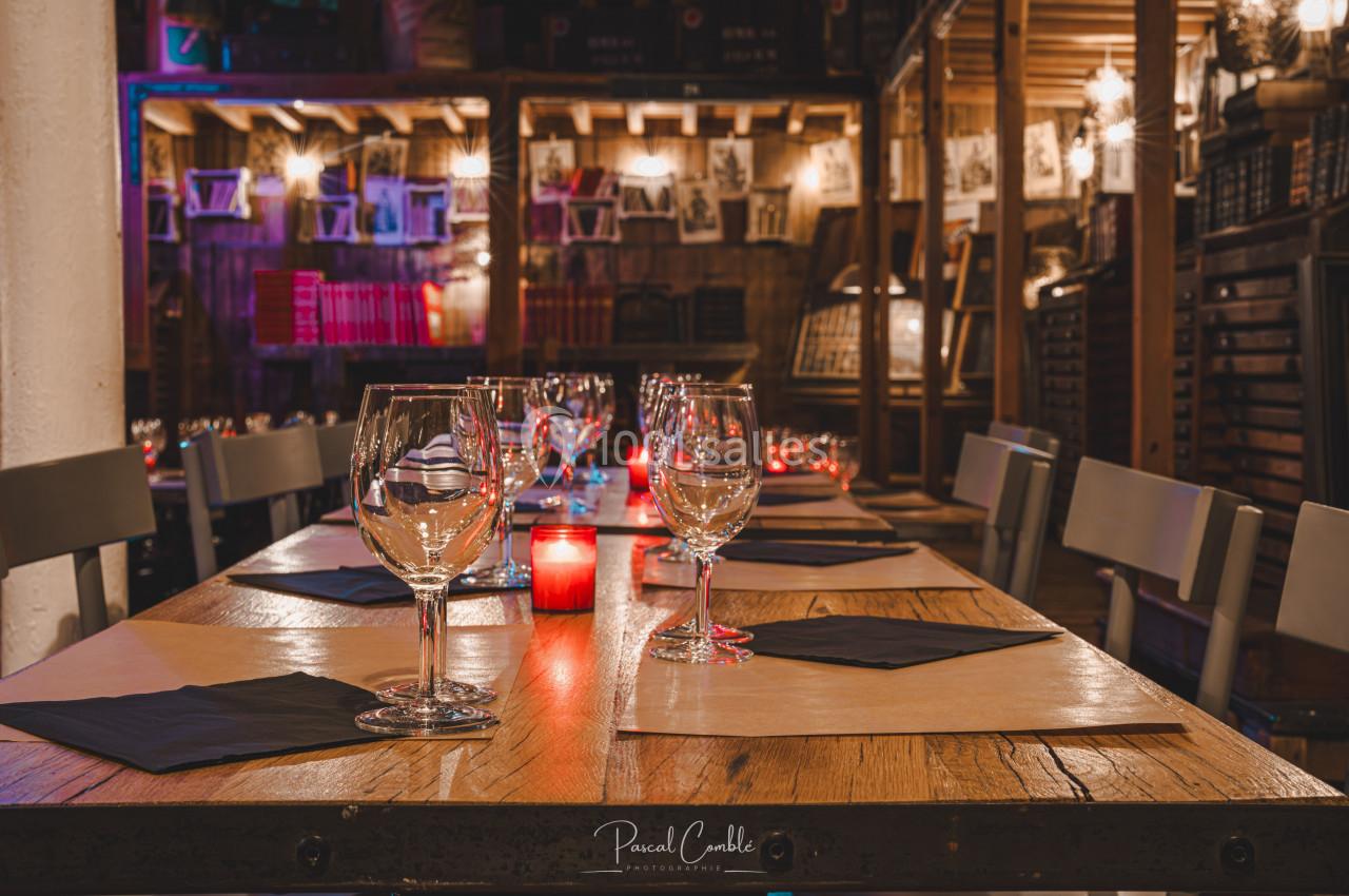 Table en bois dressée avec des verres à vin, serviettes noires et bougies rouges dans une ambiance chaleureuse.