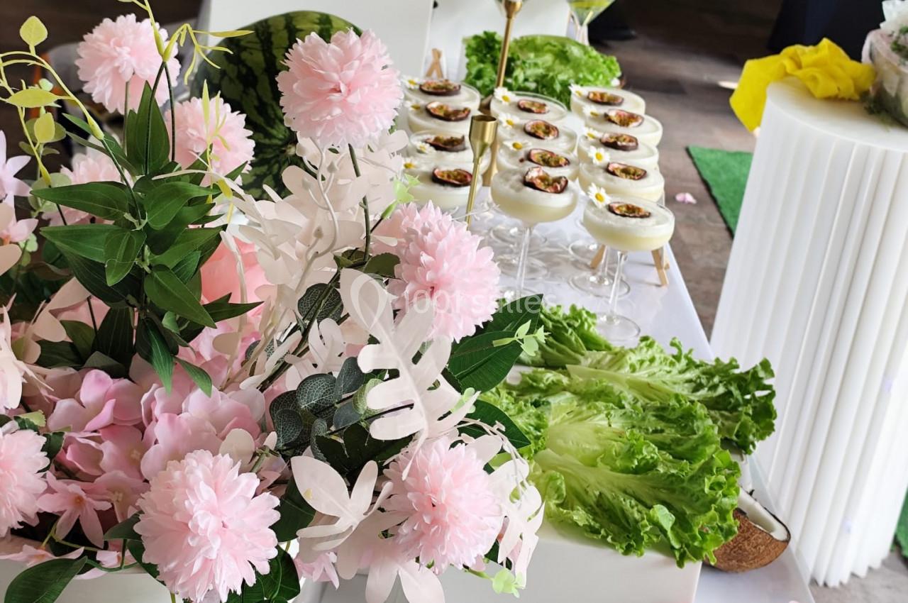 Buffet décoré avec des fleurs roses, des feuilles de laitue et des amuse-bouches disposés sur une table blanche.